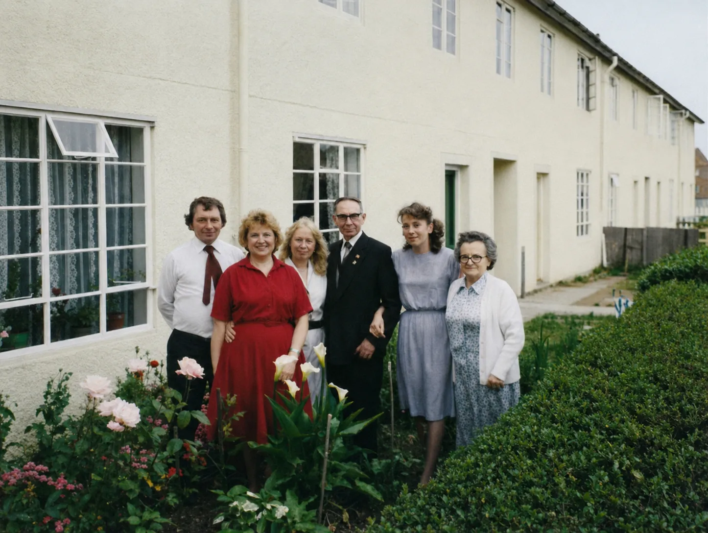A colour family photograph in front of a row of white-rendered terraced houses in Trowbridge. Antoni Czerniachowicz stands in the centre in a dark suit, wearing a lapel pin, surrounded by his family: adult children and his wife Helena beside him.