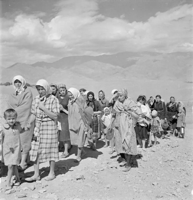 A black-and-white photograph of Polish refugees, mostly women and children, walking in a long file over bare mountain terrain, carrying bundles and suitcases, on the route from the Soviet Union into Persia in 1942.