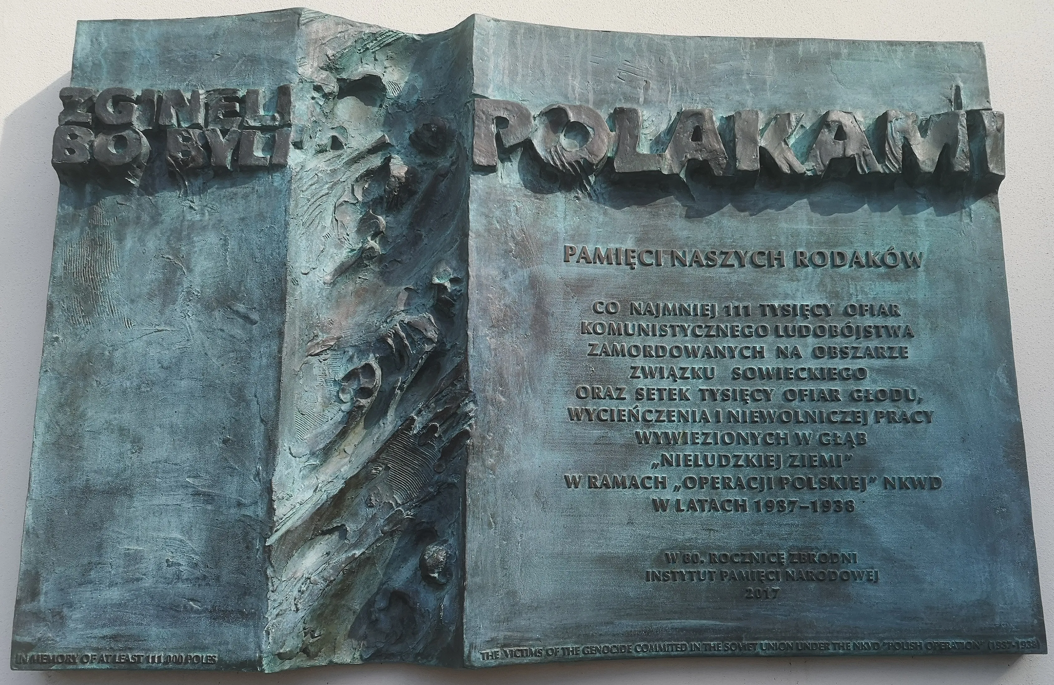 A bronze memorial plaque in Kraków, cast in the form of an open book. The left page reads 'Zginęli bo byli Polakami' ('They died because they were Poles'); the right page commemorates at least 111,000 victims of the NKVD Polish Operation of 1937–38.